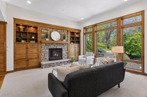 Main floor living room with 11' ceiling, soaring windows, custom built-ins and a stunning stone fireplace - the perfect blend of warmth, craftsmanship and peaceful nature views.