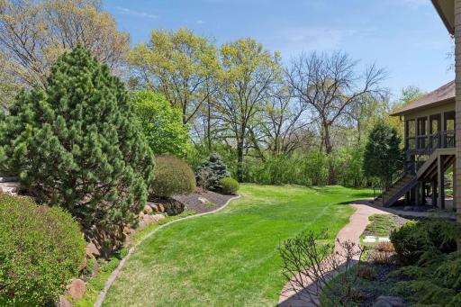 The beautifully landscaped backyard offers a private, park-like setting with mature trees, manicured lawn, and winding pathways.