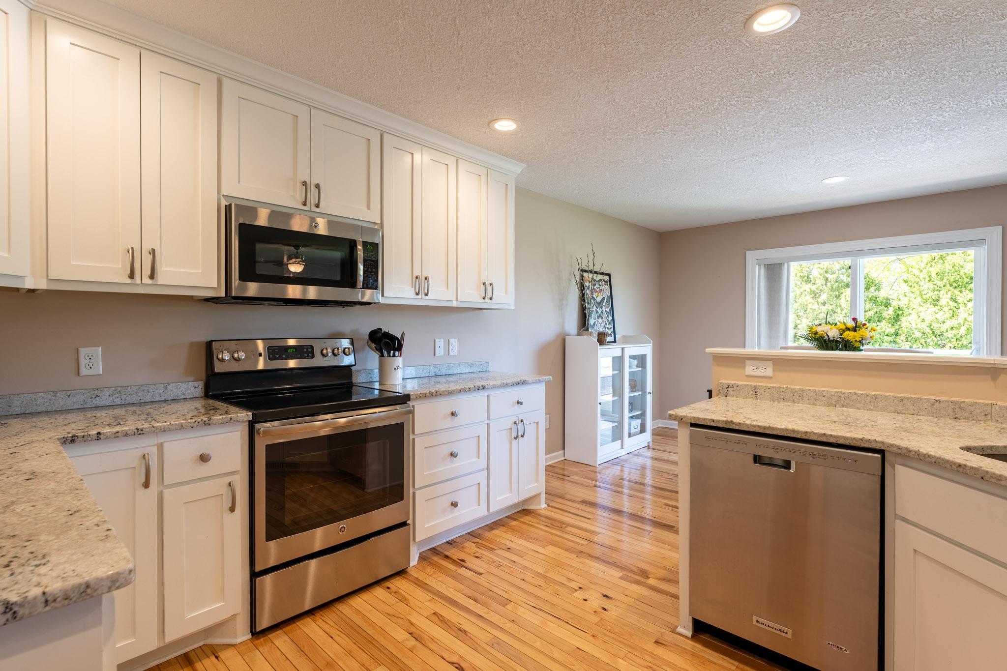 Kitchen with Hickory floors, white cabinets, granite countertops, & stainless steel appliances.