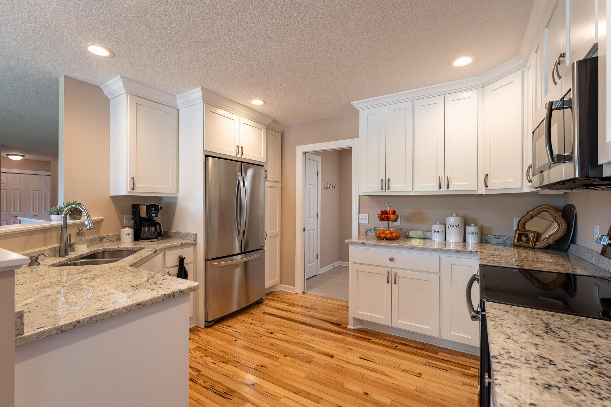 A stylish kitchen showcasing white cabinetry, granite countertops, hickory hardwood floors, and stainless-steel appliances.