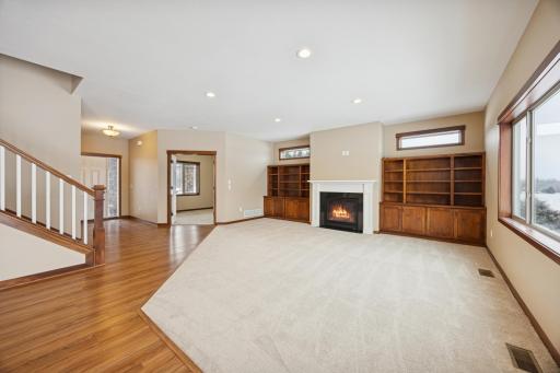 Bright and spacious main-level living room with gas fireplace, built-in shelving, and large windows overlooking the backyard.
