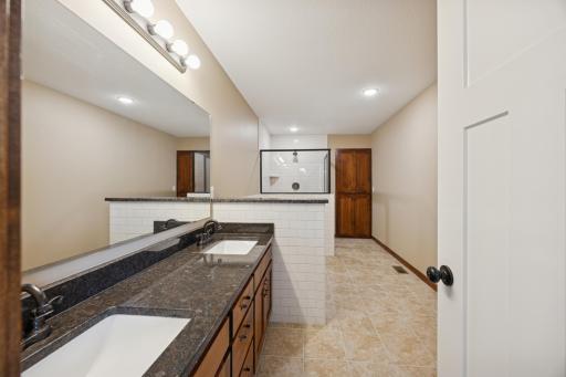Spacious primary bathroom featuring a dual-sink vanity with granite countertop, ample storage, and updated lighting.
