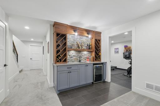 Stylish wet bar with custom cabinetry, stone backsplash, and beverage refrigerator.