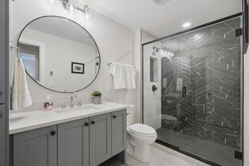 Lower-level bathroom with heated floors, custom vanity, quartz countertop, and tiled shower.