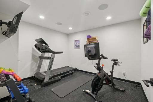 Lower-level gym or flex room with rubber flooring and glass doors.
