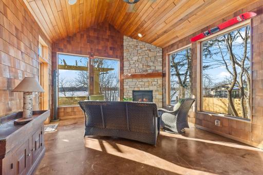 Three season porch with stained concrete flooring, cedar shake walls and floor to ceiling stone surround on gas fireplace.