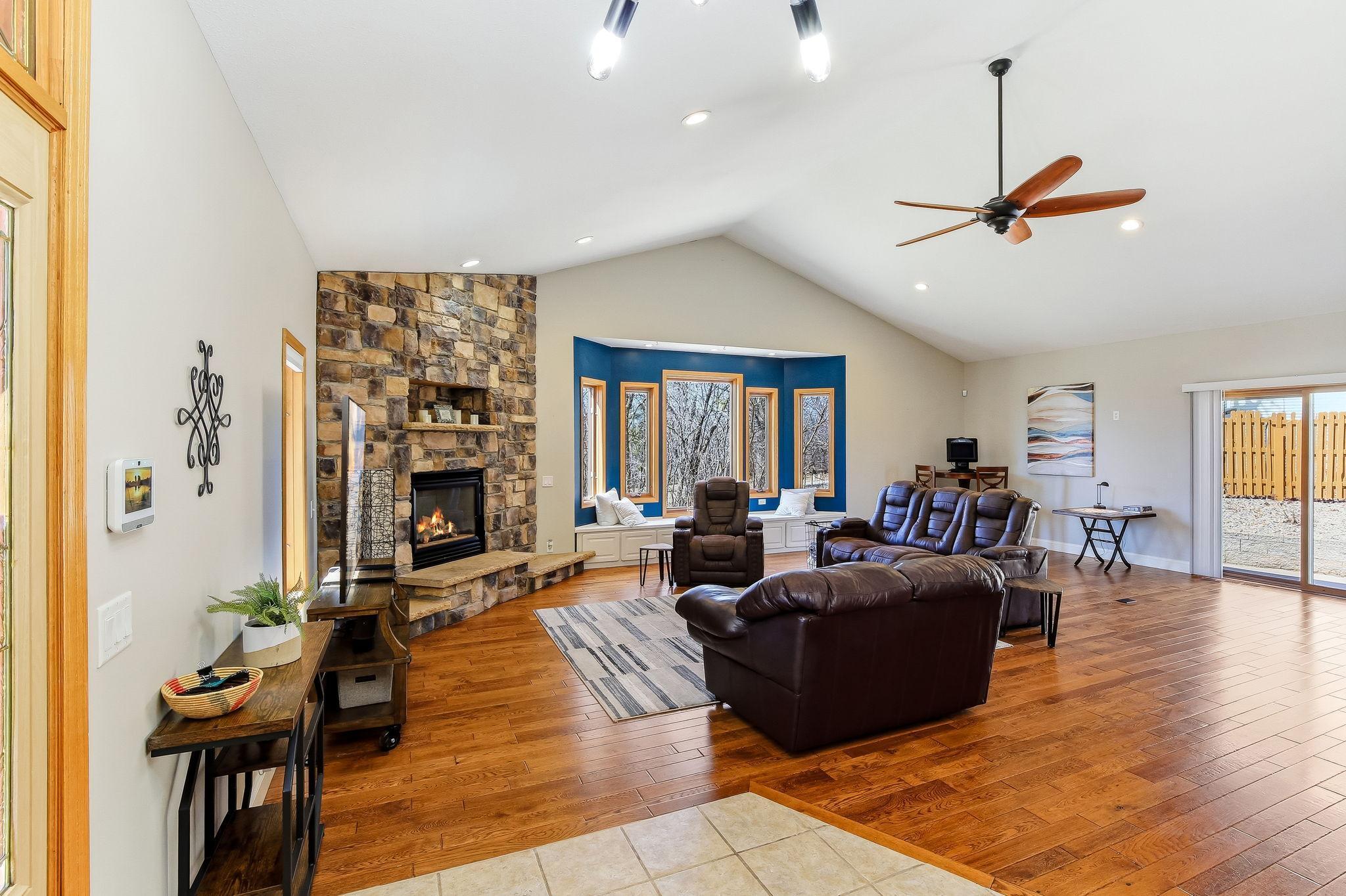 Vaulted Great Room with wood floors, full wall stone Fireplace, and abundant natural light.