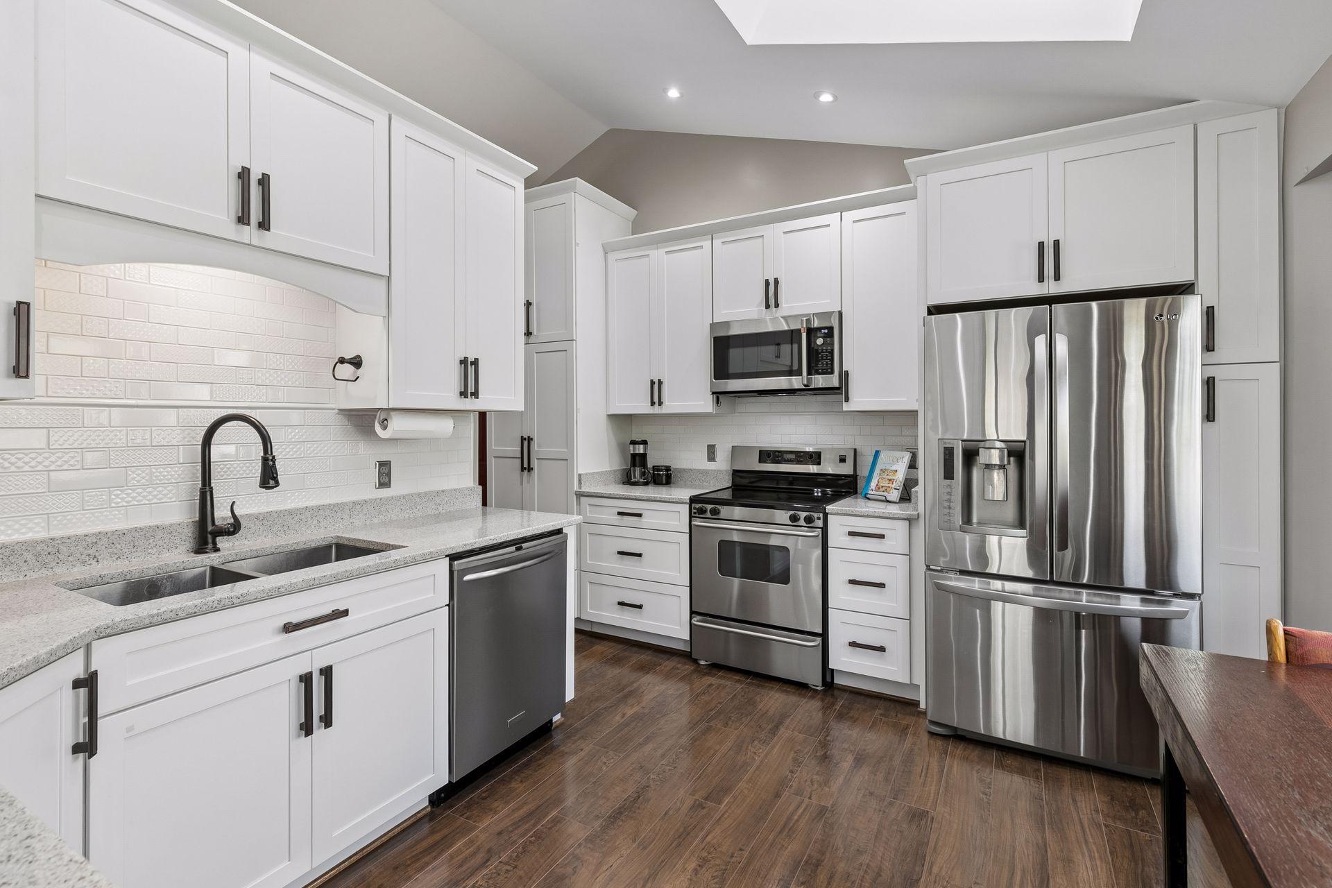 Fully remodeled kitchen featuring white custom cabinetry, quartz-style countertops, subway tile backsplash, stainless steel appliances and abundant cabinet storage.