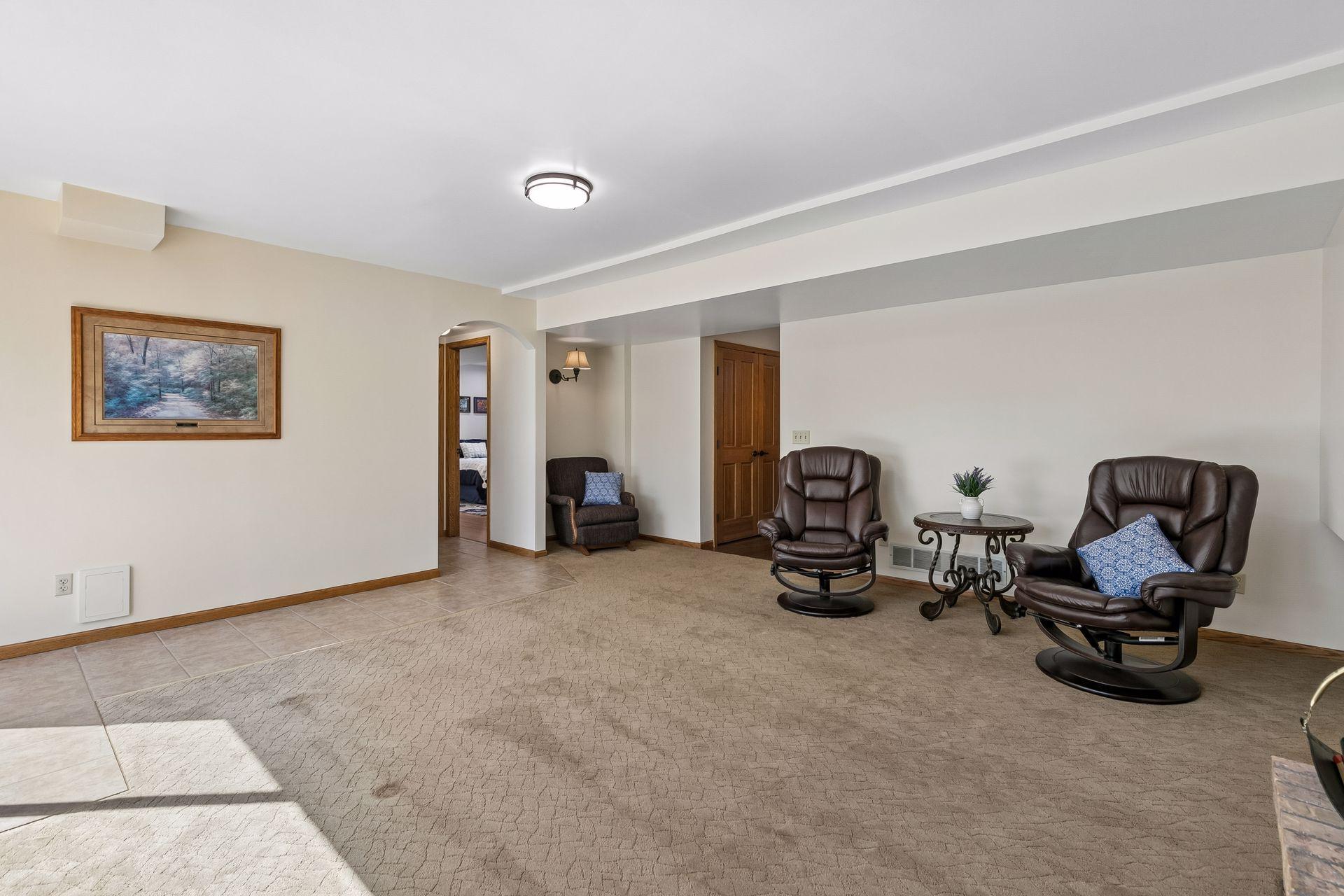 Another view of the spacious lower-level family room featuring a cozy wood-burning fireplace, open layout, and flexible space for entertaining, movie nights, game area, or additional seating.