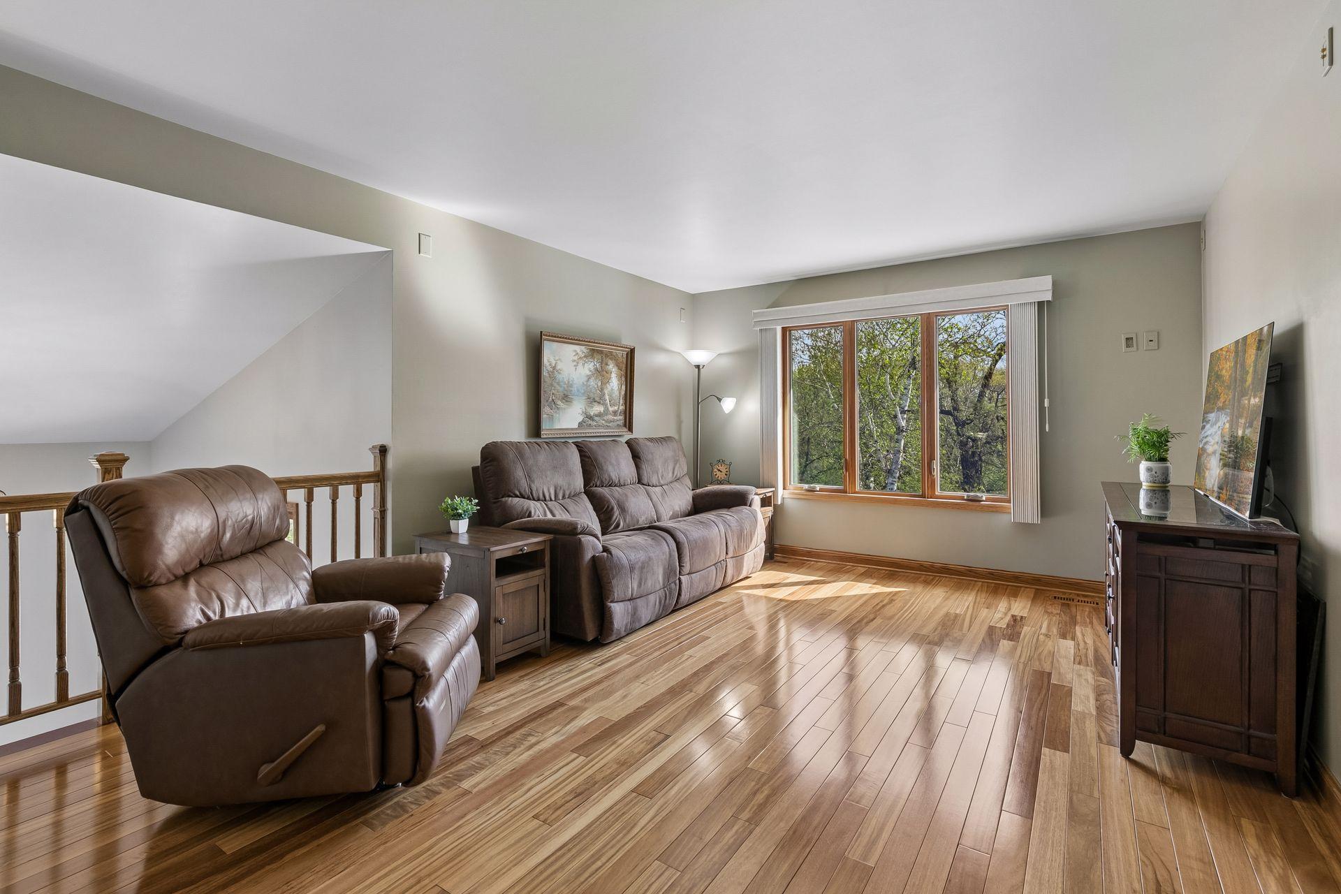 Spacious upper-level living room with oversized windows, beautiful natural light and peaceful wooded views, creating a warm and inviting gathering space.