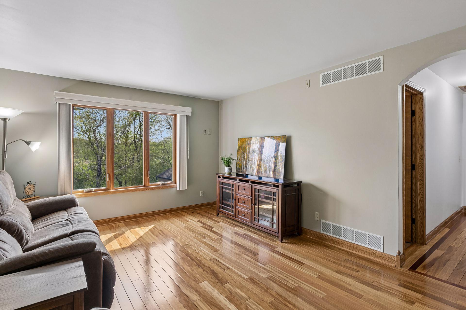 Bright open living area featuring updated hardwood-style flooring, large picture window and scenic backyard views, ideal for relaxing, entertaining or family movie nights.