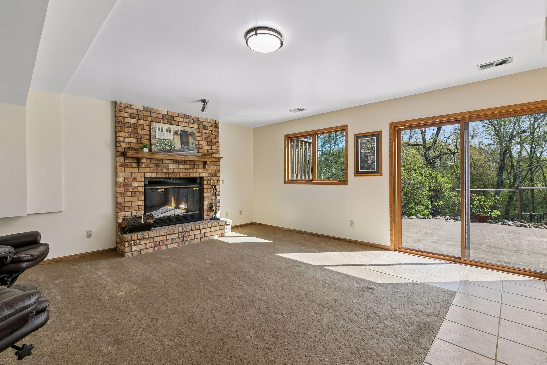 Spacious lower-level family room with cozy wood-burning fireplace, large windows, and walkout access to the backyard patio- perfect for entertaining, movie nights or relaxing gatherings.