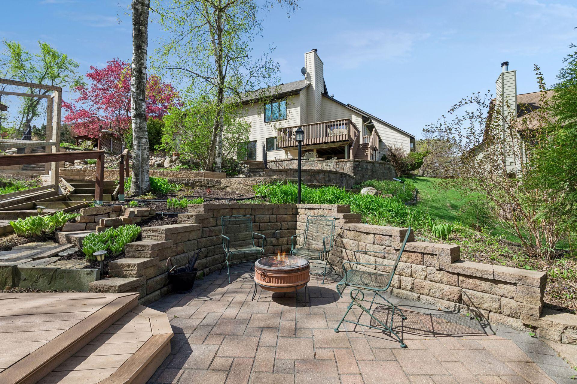 Cozy firepit patio surrounded by professional landscaping, retaining walls, and multiple seating areas - perfect for evenings outdoors with family and friends.
