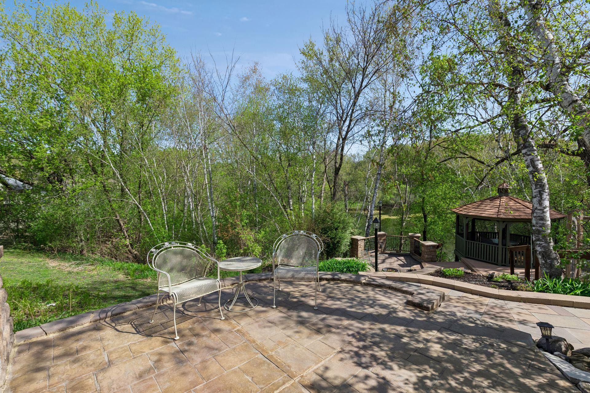 Private paver patio surrounded by mature trees, peaceful nature views, and beautifully landscaped outdoor living spaces - perfect for morning coffee or relaxing evenings outdoors.