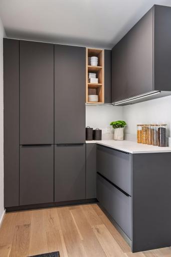 This stunning walk-in butler's pantry features floor-to-ceiling custom cabinetry in sophisticated charcoal with soft-close European hinges, complemented by an elegant white oak open shelving.