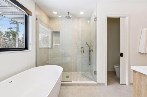 Serene primary bedroom with abundant natural light and private bath access. Soaking tub positioned beneath picture window for ultimate relaxation.