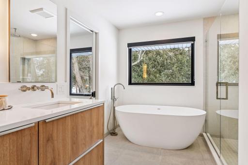 Spa-inspired primary bath with freestanding soaking tub and frameless glass shower. This designer primary bathroom rivals five-star resort with custom white oak vanities.