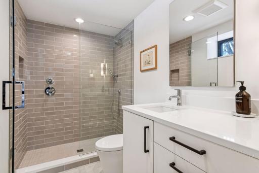 Spa-like guest bath with floor-to-ceiling tile and frameless glass enclosure showcases designer tile, quartz counters, and premium fixtures.