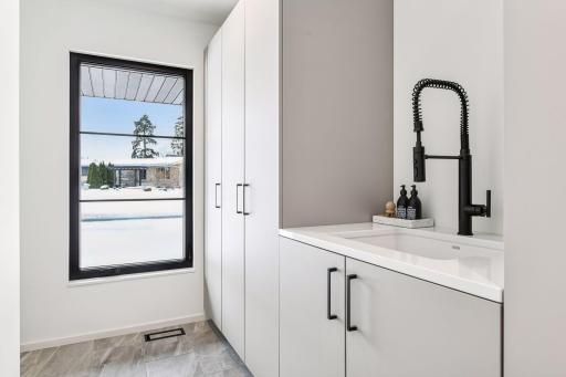 Elegant main-floor laundry room features floor-to-ceiling custom white cabinetry, pristine quartz countertops, and a professional-grade utility sink with matte black fixtures. This thoughtfully designed space elevates everyday chores.