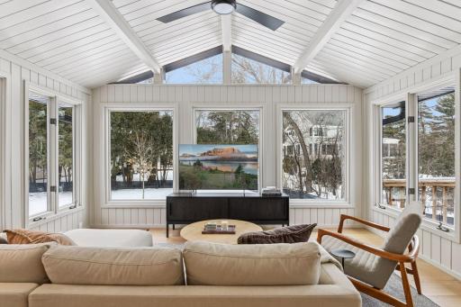 Stunning sunroom with cathedral ceilings, clerestory windows, and walls of glass that blur the lines between indoor comfort and outdoor beauty year-round. This light-drenched retreat features pristine white shiplap walls and direct access to the deck