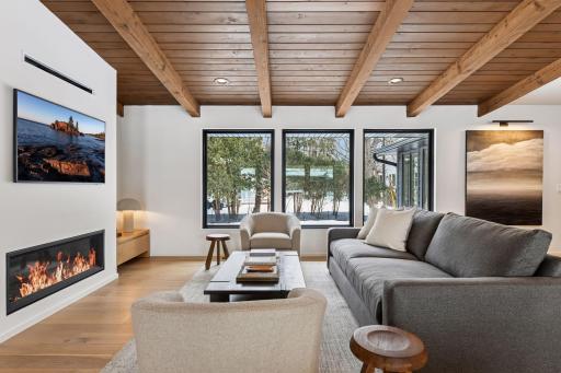 Soaring natural pine beamed ceilings anchor the light-filled great room. Walls of windows frame serene wooded views throughout open living area.
