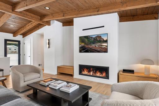 The heart of this completely renovated masterpiece centers on a sophisticated linear fireplace set into a pristine white feature wall, commanding attention beneath soaring vaulted ceilings.