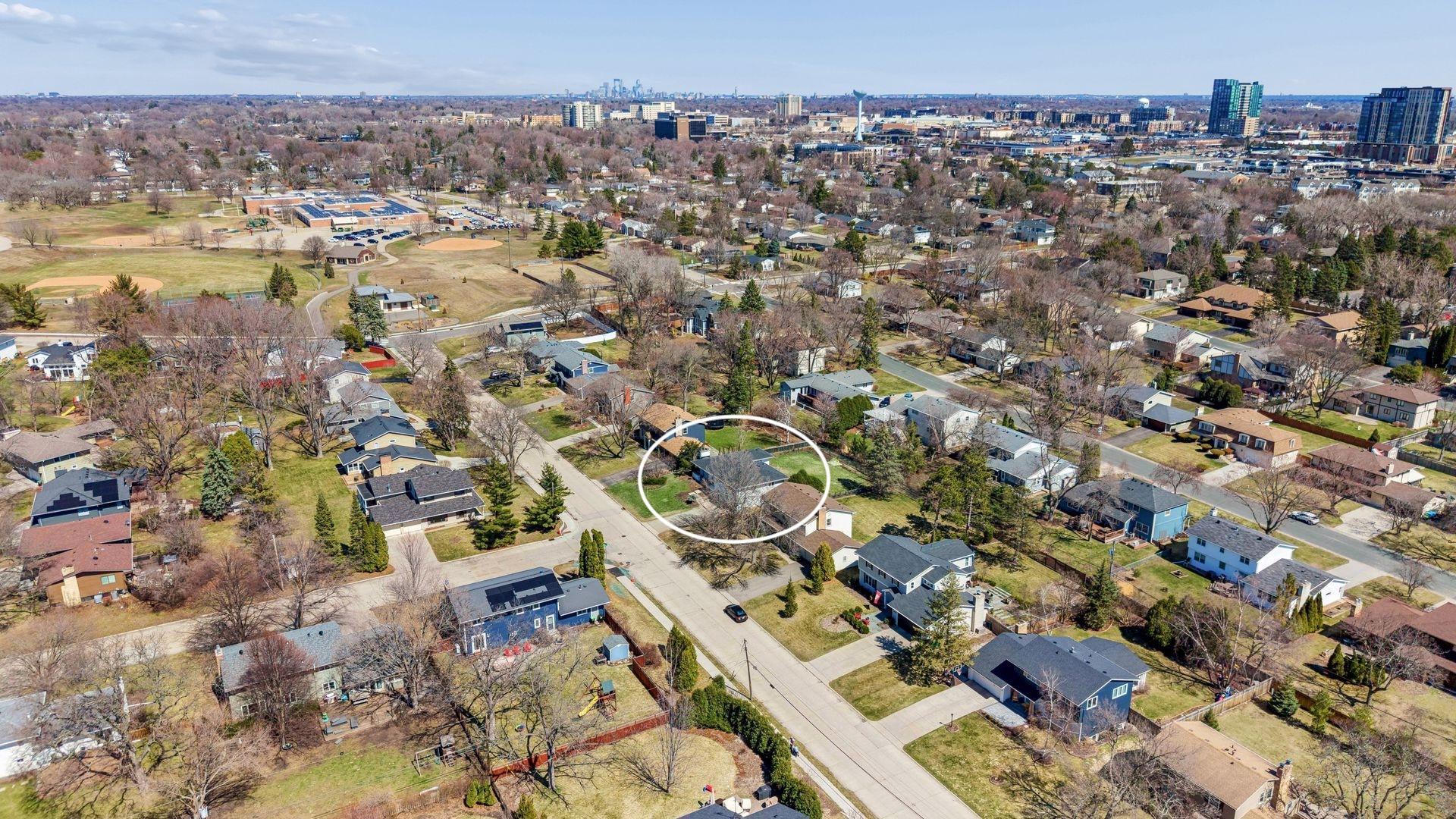 Aerial view looking down Oaklawn Avenue, with Cornelia Elementary School at the end of the block, countless shops and amenities along France Avenue and the Minneapolis skyline in the background.