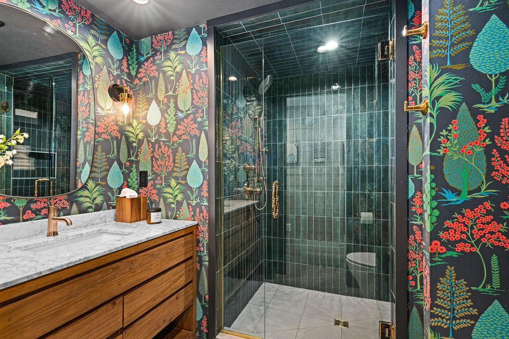 Newly added 3/4 bathroom with a tiled floor and walls, marble top vanity, and built in shelving.