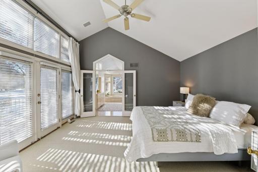 The main floor Primary Bedroom walks out to its own private deck. The Primary Bath en suite is visible past the double glass doors.
