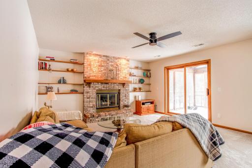 Cozy lower-level family room featuring a charming brick fireplace, built-in shelving, and direct access to the screened porch.