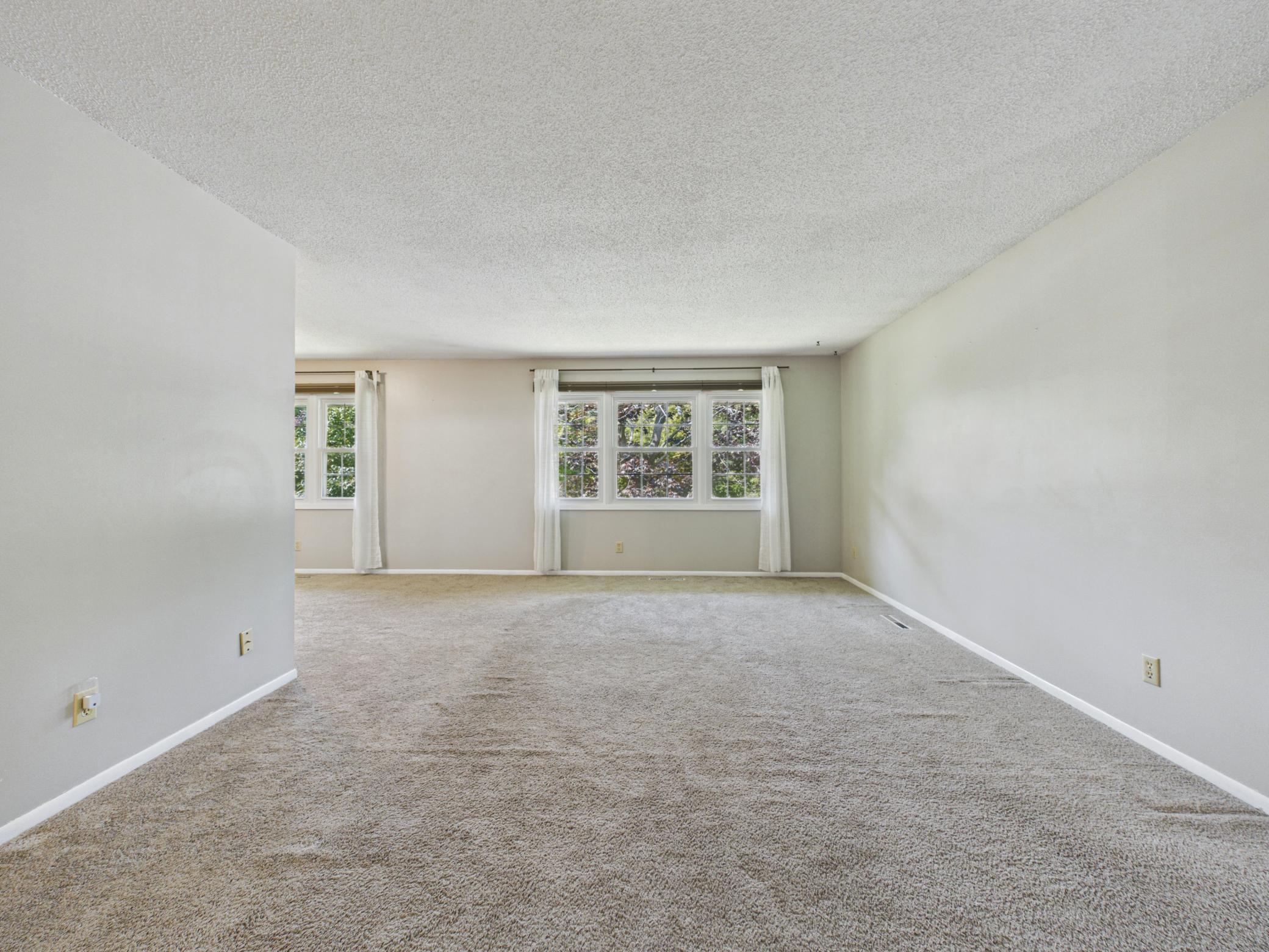 Spacious and welcoming main floor living room with plush carpet, generous room for the whole family, and an open flow into the dining room and kitchen. A warm and comfortable space perfect for everyday living and entertaining alike.