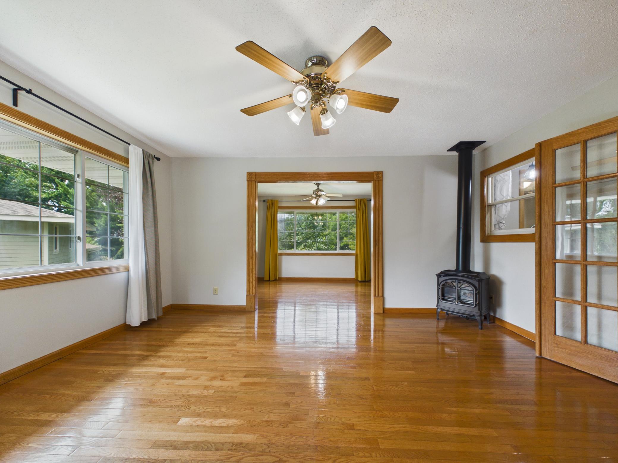 Spacious living room with hardwood floors, ceiling fan, and gas stove — opens to a bright dining room.