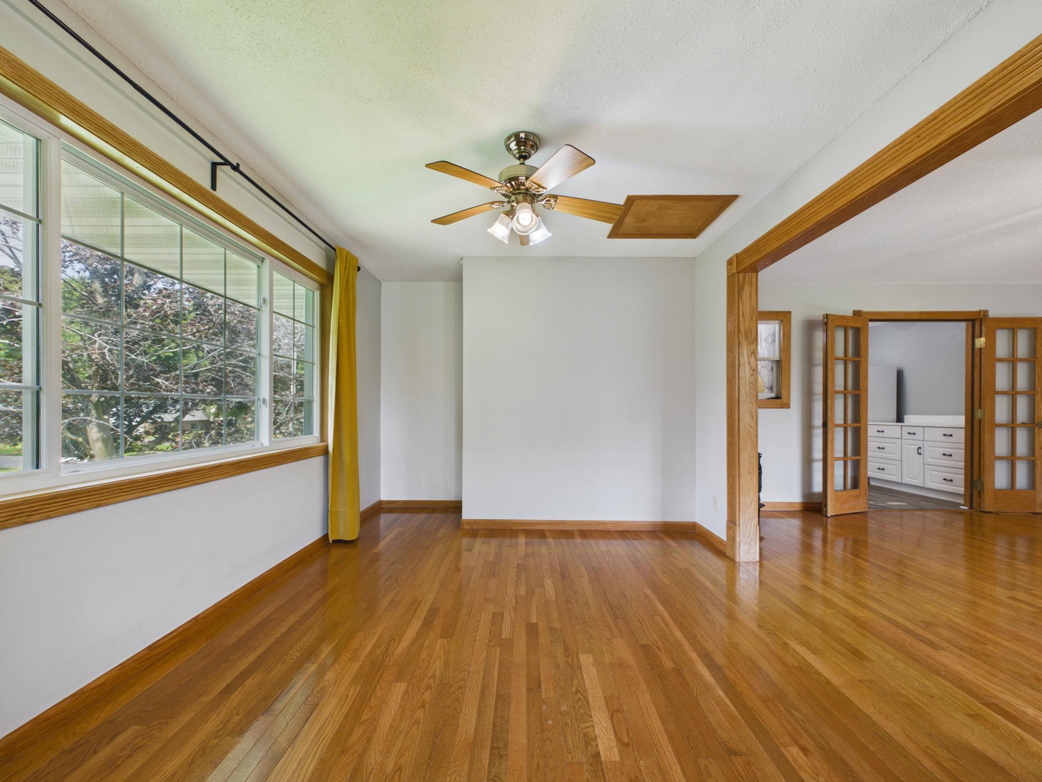 Spacious living room with hardwood floors, ceiling fan, and gas stove — opens to a bright dining room.