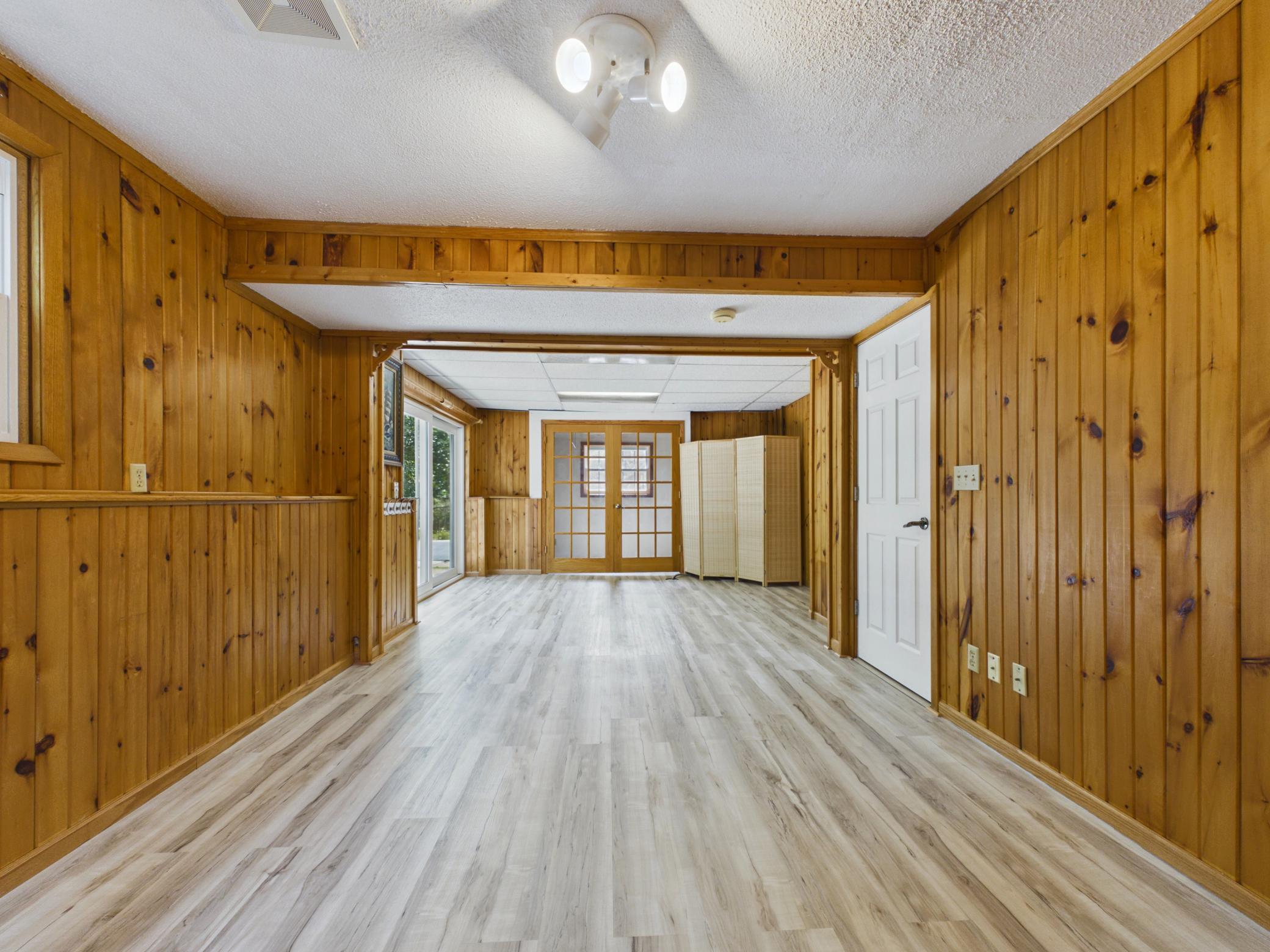 Spacious lower-level rec room with knotty pine walls, new vinyl plank flooring, and a walkout to the backyard — laundry room tucked behind the French doors. Plenty of room for a pool table or game area.