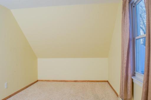 Bedroom with sloped ceiling, window, and carpeted flooring.