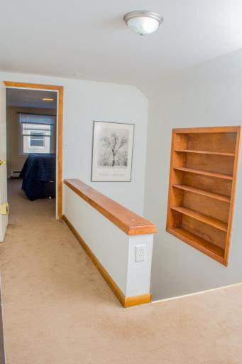Hallway with carpeted flooring, wood trim, and built-in wall shelving.