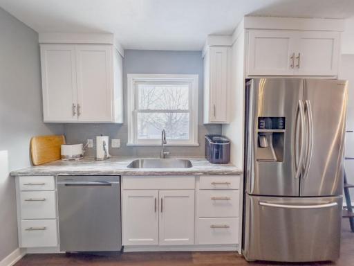 Updated kitchen featuring white cabinetry, solid-surface counters, stainless steel sink, and window above the sink.