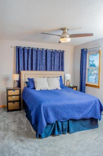 Spacious bedroom with carpeted flooring, ceiling fan, and windows on two walls.