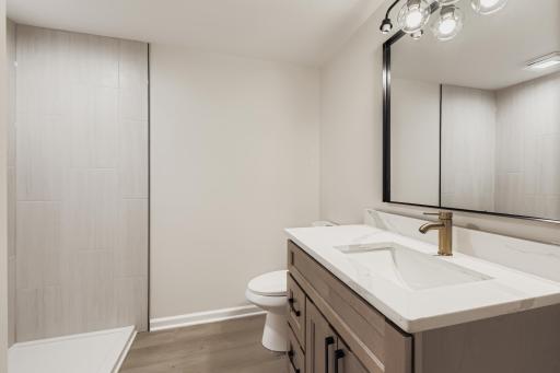 Lower-level 3/4 bath with matching cabinetry, built-in shelves, and separate shower lighting.