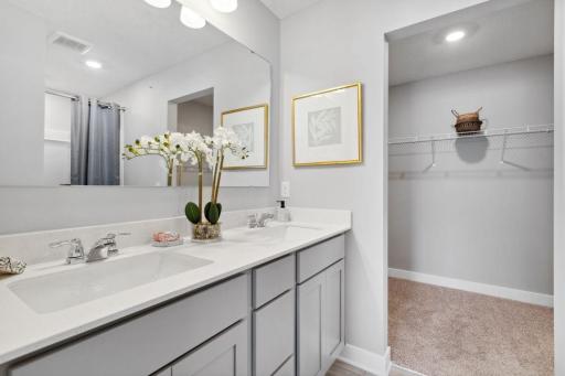 A peak inside the bathroom off the Primary Suite. Notice the extra high cabinets and double-bowl Quartz covered vanity with loads of storage! Photo is of model home. Colors and options may vary. Ask Sales Agent for details.