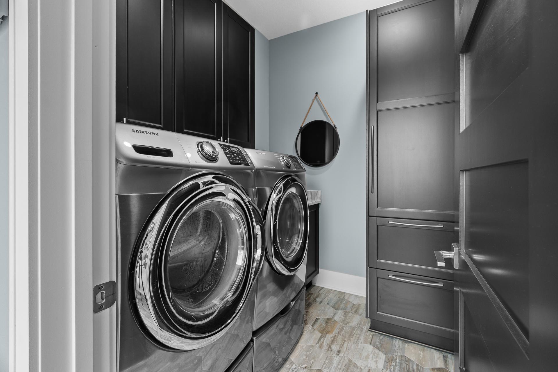 The Laundry Room connects to the primary walk-in closet and kitchen hallway. Complete with storage cabinets and a utility sink (under the mirror).