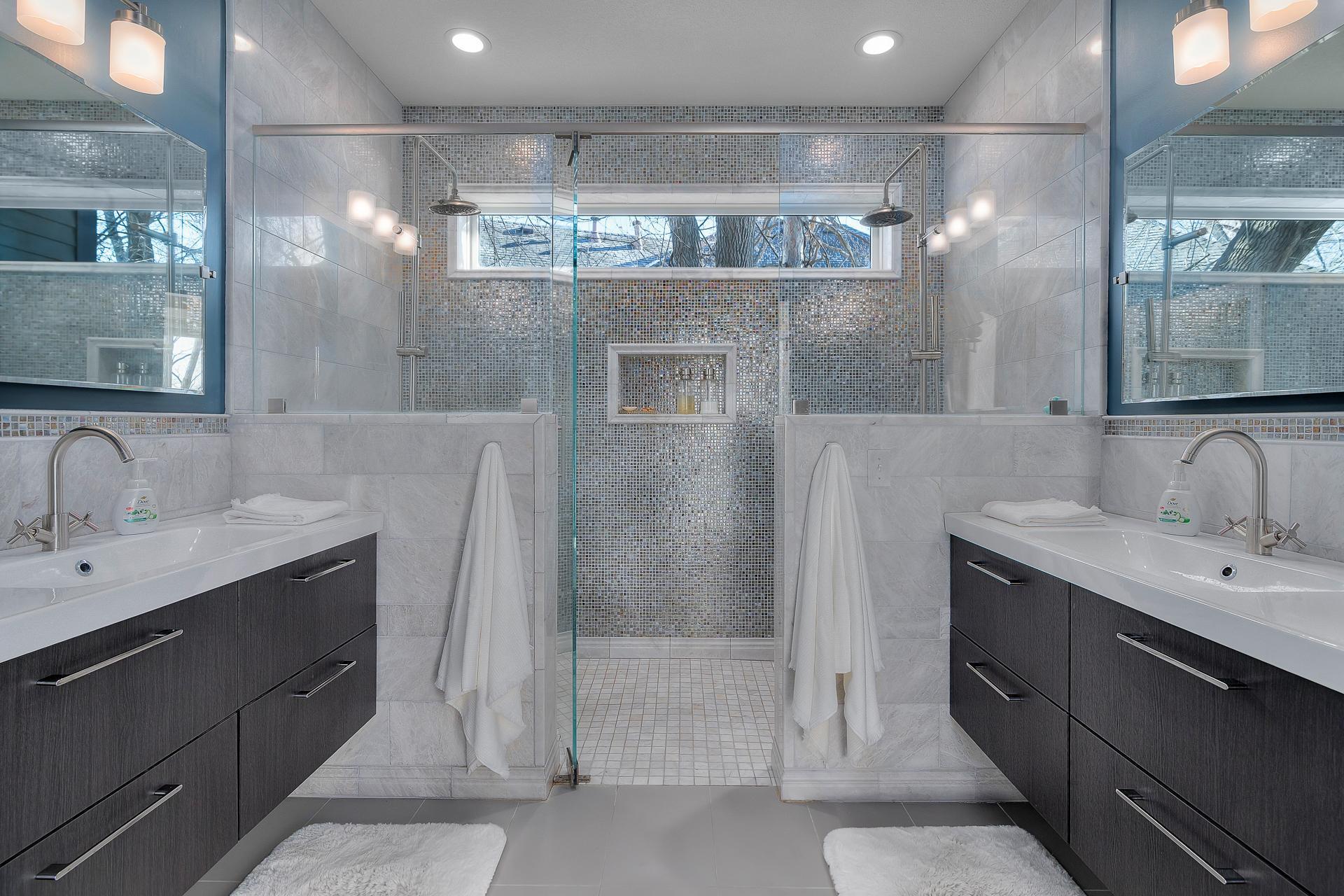 Primary bath features a dual shower with floor to ceiling custom tile walls and heated tile floor, dual floating vanities, custom tile, and private toilet.