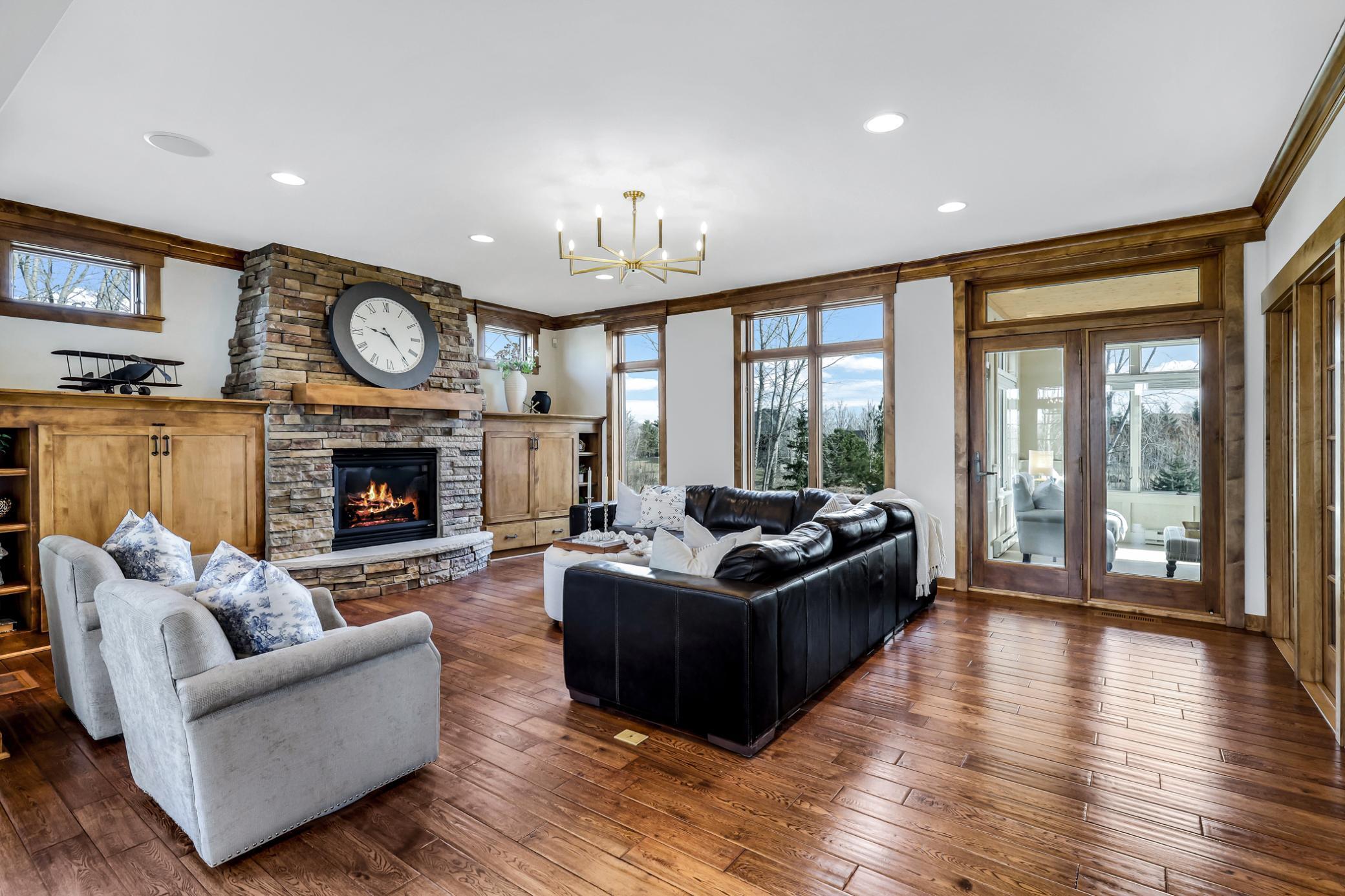 Gas fireplace with stacked stone surround from floor to ceiling, stone hearth, timber mantel, and flanking media built-ins with upper transom windows.