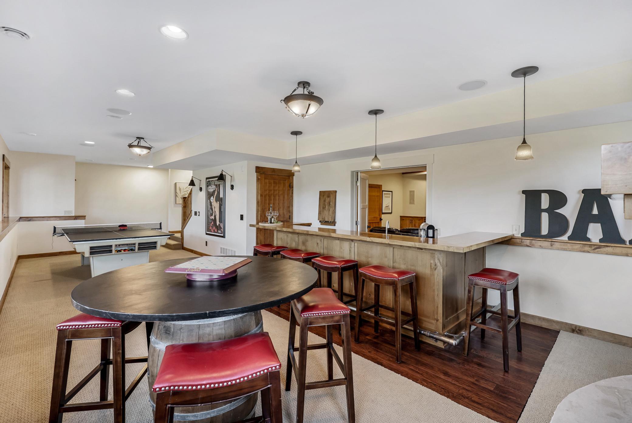 Handsome sit-down bar with seating for 5+ featuring natural wood cabinetry and raised bar, granite counters, sink, 2 beverage fridges, ice maker, and luxury vinyl plank flooring w/stainless footrest around the bar.