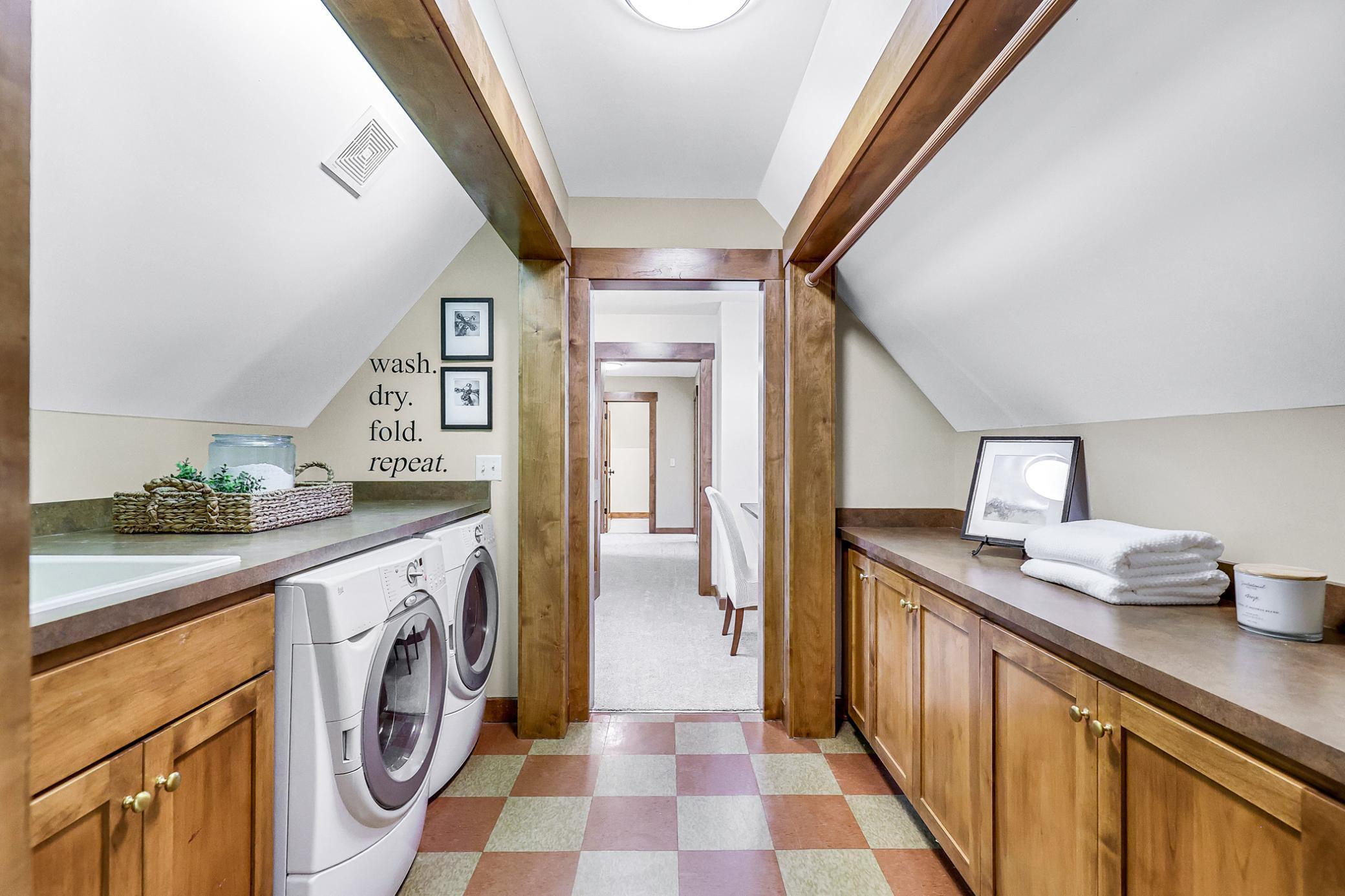 Accessed via a pocket door near the primary suite, its open galley design features washer, dryer, sink & counter on one side, while the other offers storage, folding counter & drying rack.