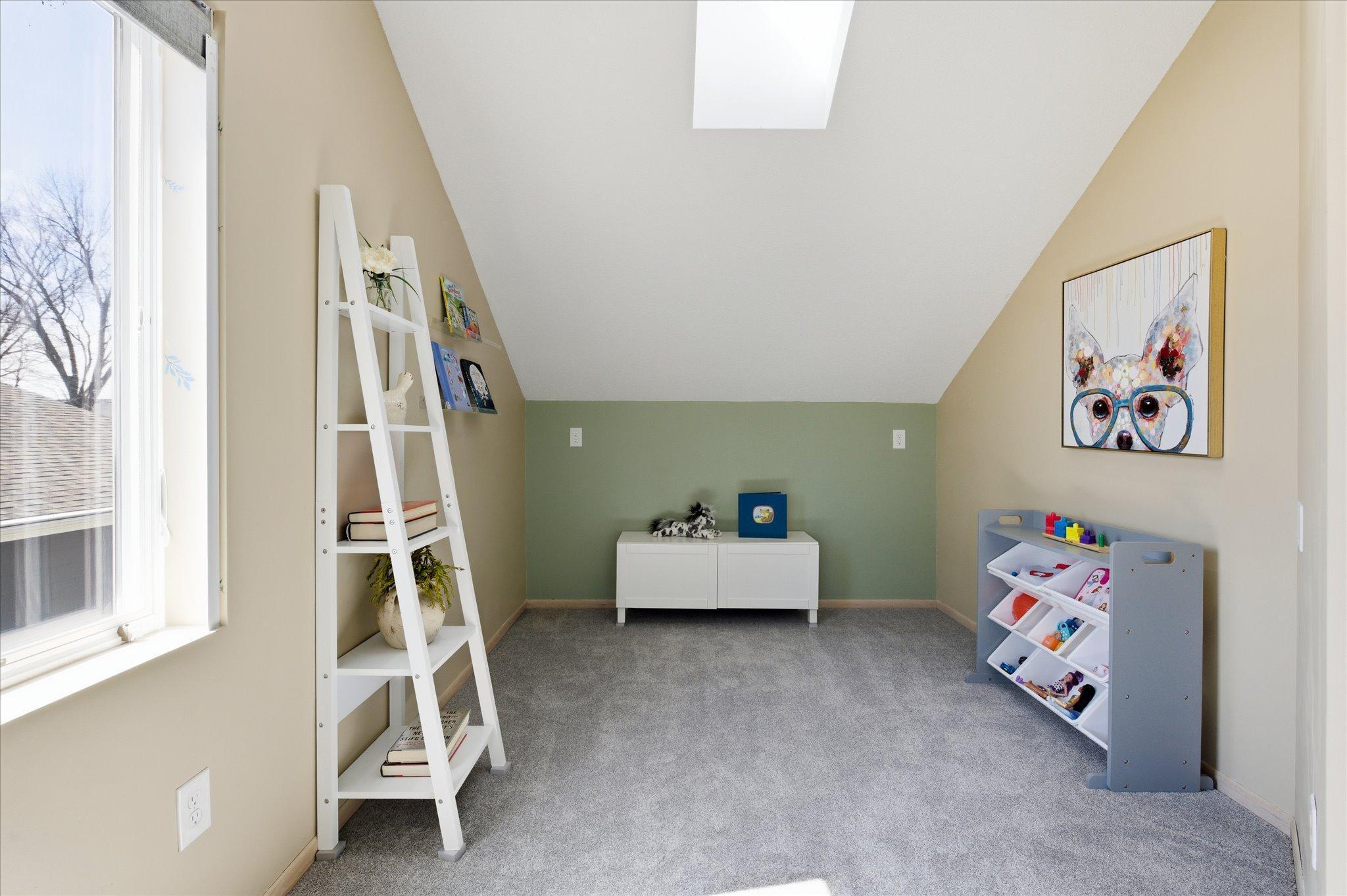 Light-filled upper-level bedroom with vaulted ceilings and skylight, perfectly suited as a cozy child’s room, nursery, or creative play space.