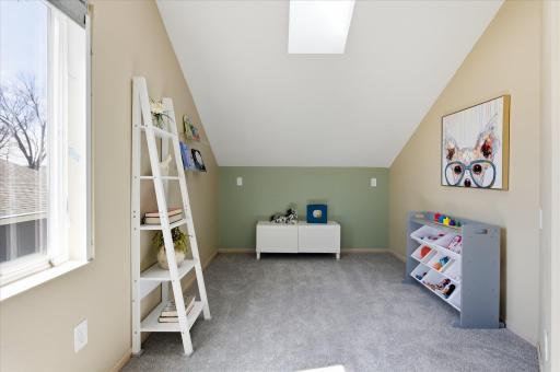 Light-filled upper-level bedroom with vaulted ceilings and skylight, perfectly suited as a cozy child’s room, nursery, or creative play space.