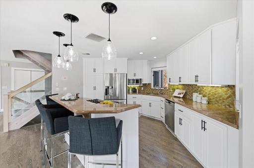 Updated kitchen featuring white cabinetry, granite countertops, tile backsplash, and stainless steel appliances.