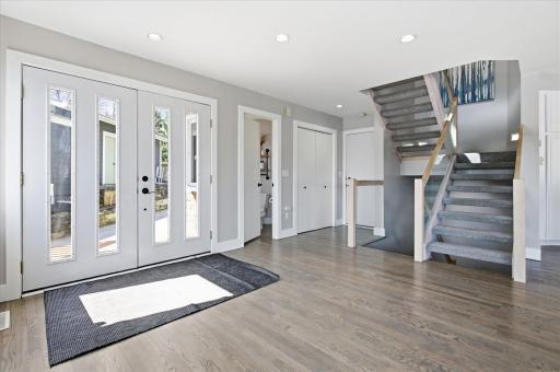 Bright and welcoming foyer with double front doors, sidelight windows, and open staircase with glass panel accents.