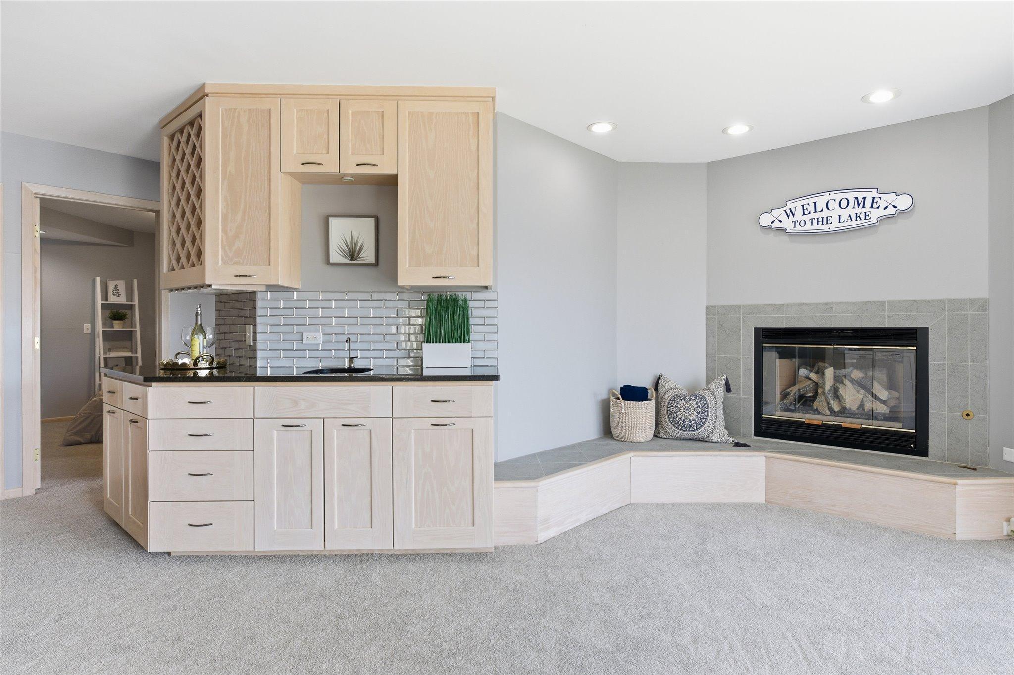 Lower-level entertaining area with built-in wet bar, cabinetry, and tile-surround gas fireplace.